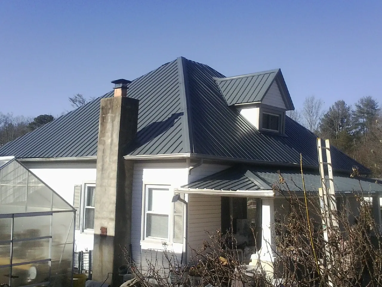 Dark blue standing seam metal roof on a white farmhouse with dormer — Slate & Tile Roof Repair by Roofing Brothers in Shaw Afb
