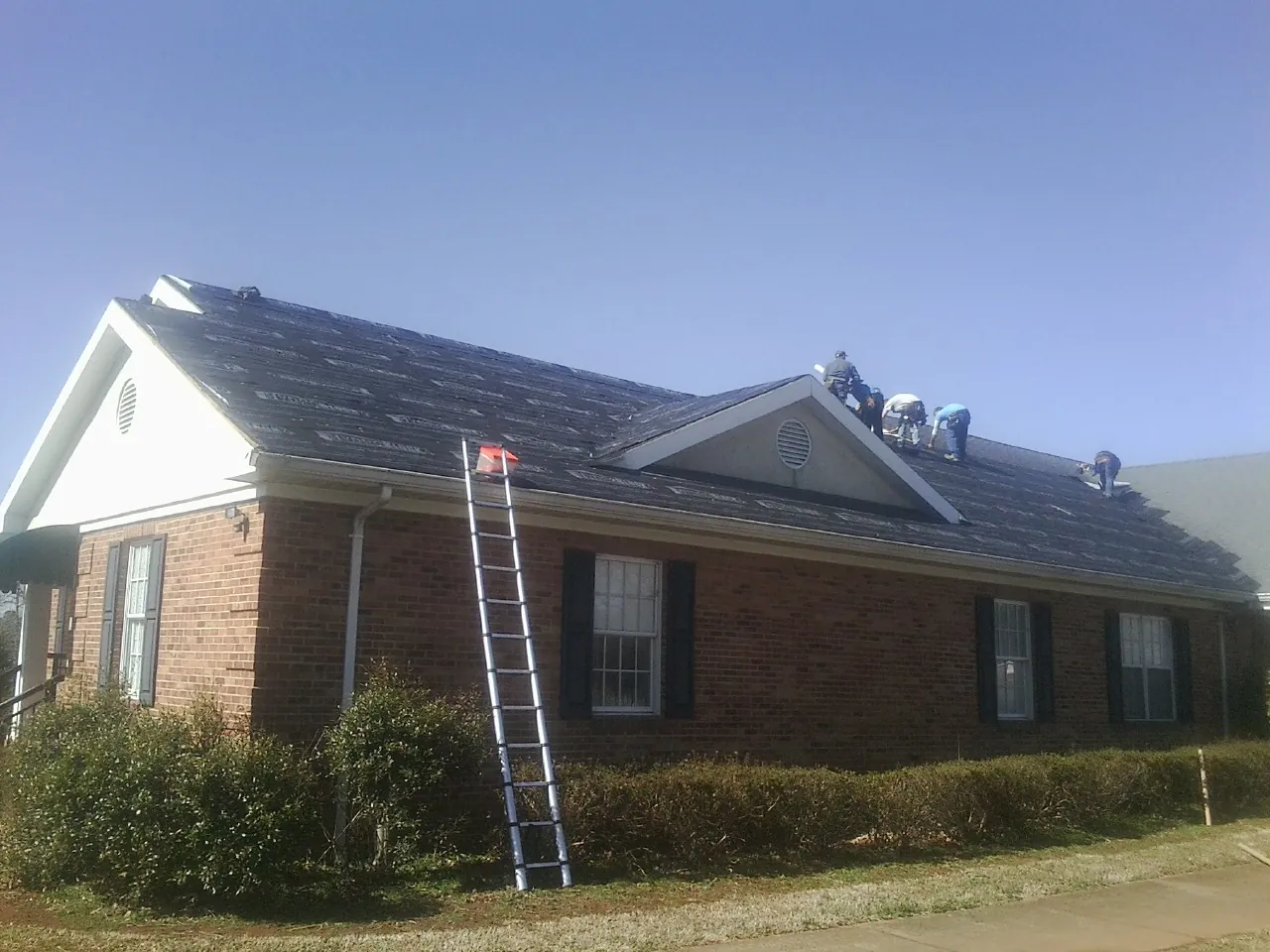 Crew tearing shingles off a brick ranch roof with a ladder set — Metal Roof Repair work by our crew in Shaw Afb