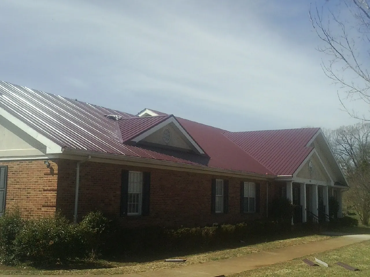 Red metal roof with gabled entries on a long brick building, from a Hail Damage Roof Repair job in Shaw Afb
