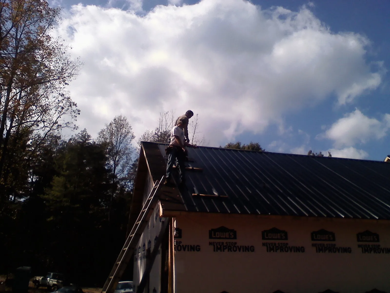 Roofer fastening dark metal panels high against a cloudy sky, from a Roof Inspection job in Shaw Afb